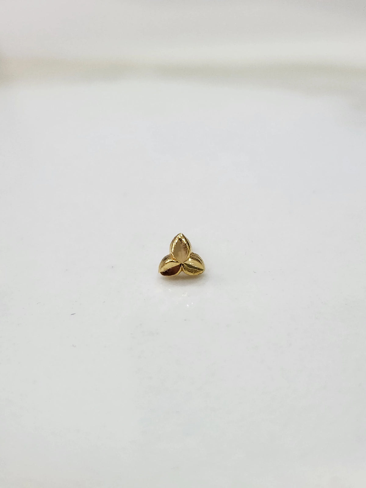 Simple gold nose pin design minimal three leaf pattern on white surface