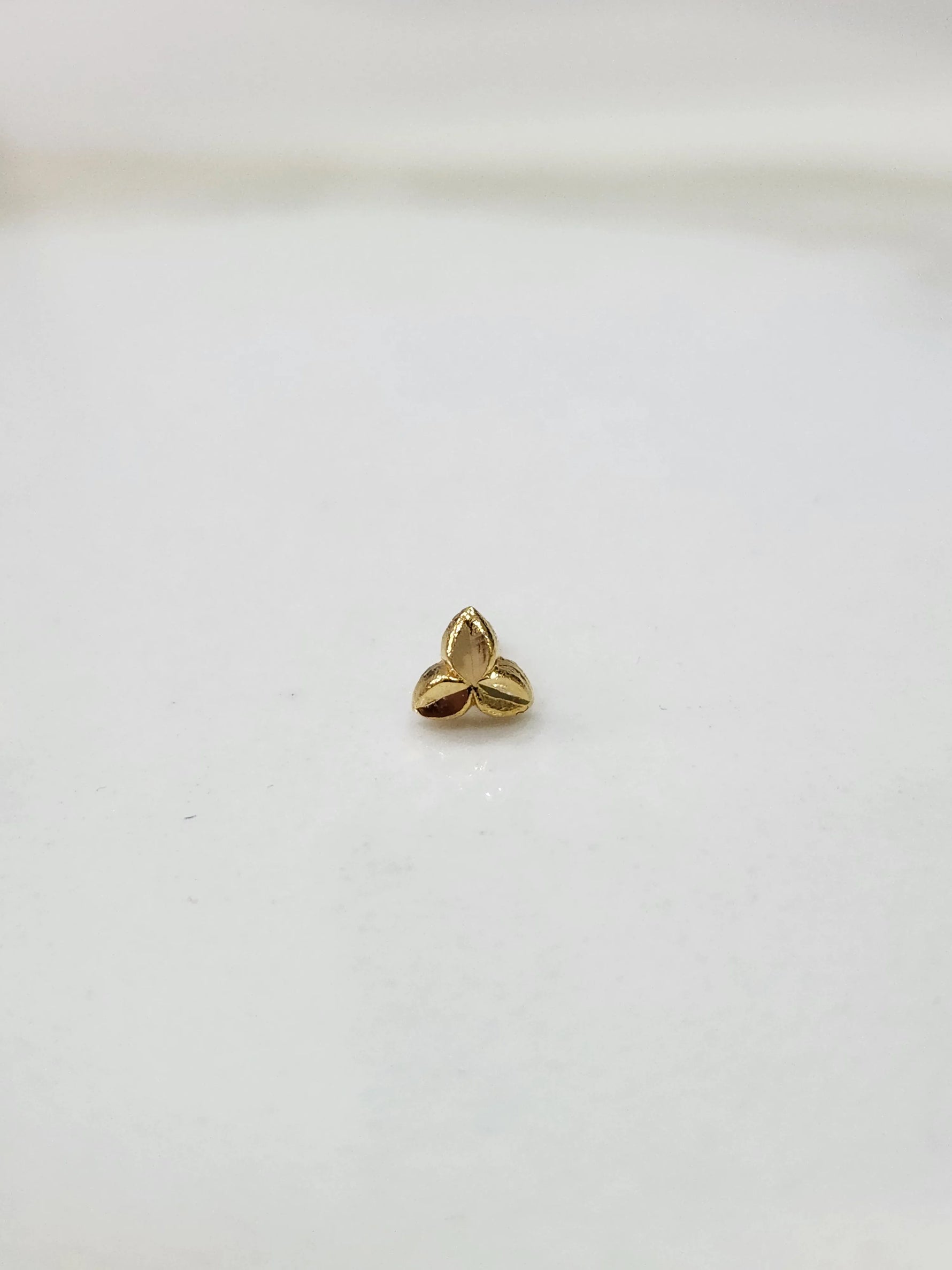 Simple gold nose pin design minimal three leaf pattern on white surface