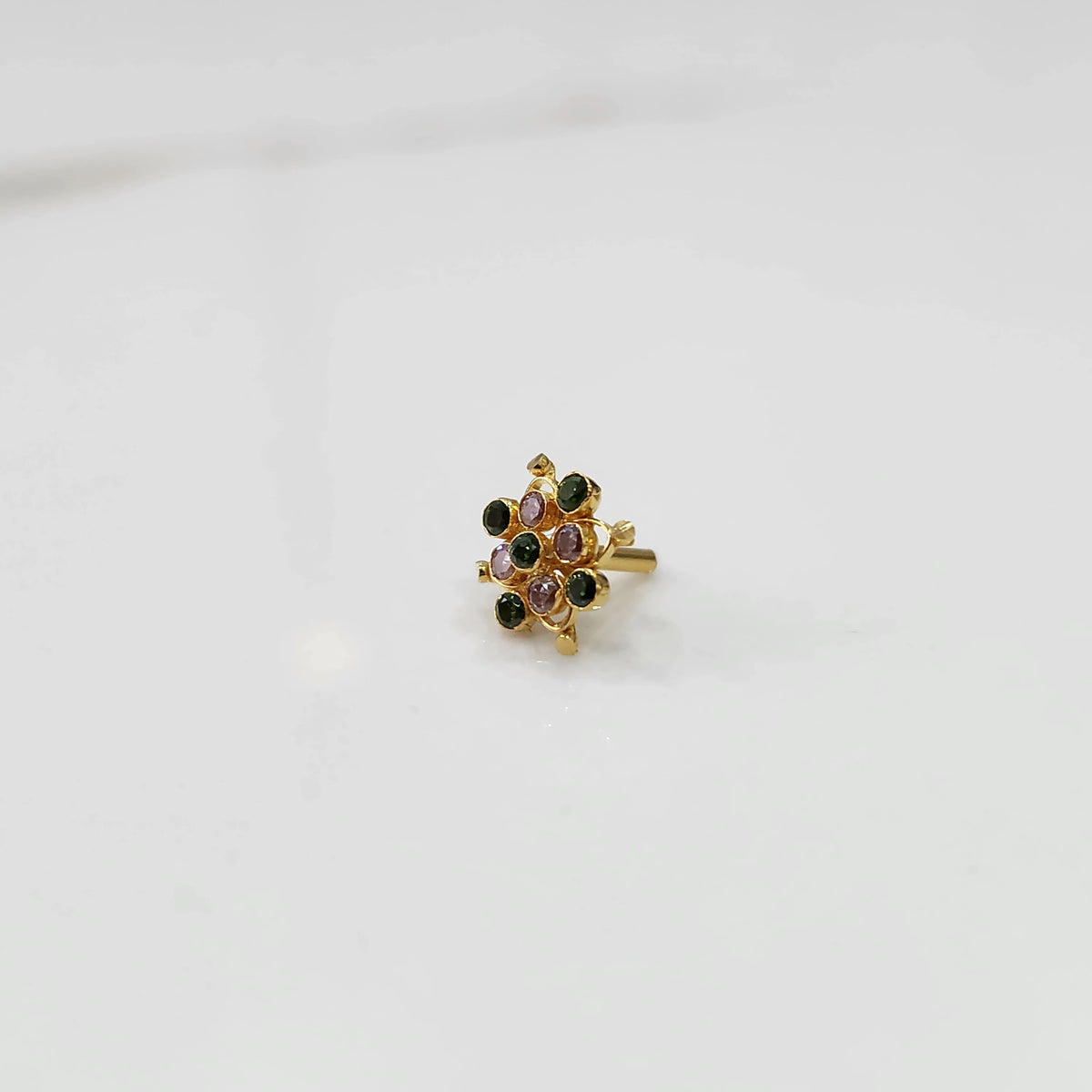 Mini stone gold nose pin floral design top view on white surface