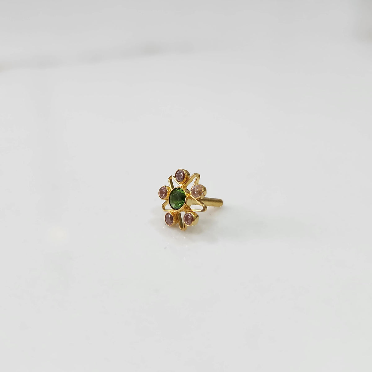 A gold nose pin shaped like a star with a green center stone and purple-pink accent stones, angled view