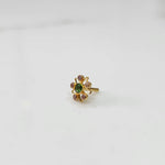A gold nose pin shaped like a star with a green center stone and purple-pink accent stones, angled view