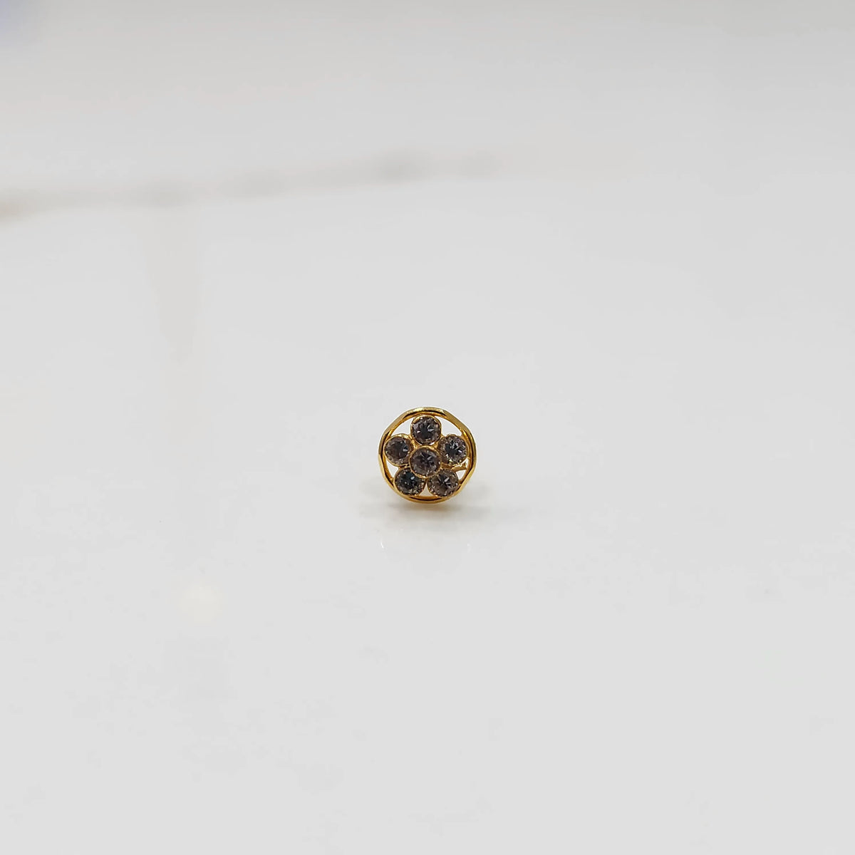 Product shot of a round gold nose stud with grey gemstone flower cluster