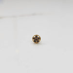 Product shot of a round gold nose stud with grey gemstone flower cluster