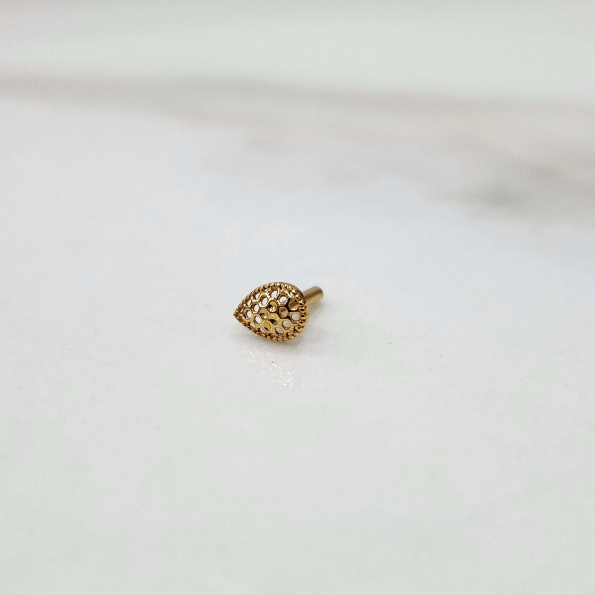 Close up of handcrafted teardrop gold nose pin design on white background elegant and modern in style