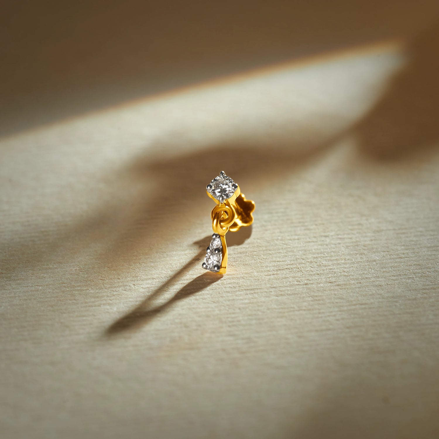 Gold nose pin design with a delicate vertical pattern featuring sparkling stones set in a polished gold base on a soft neutral background
