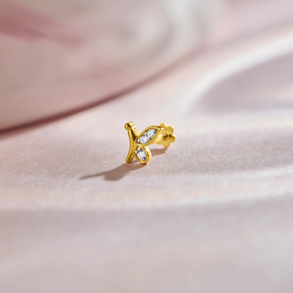 Nose pin of gold with butterfly inspired diamond design on soft pink fabric background