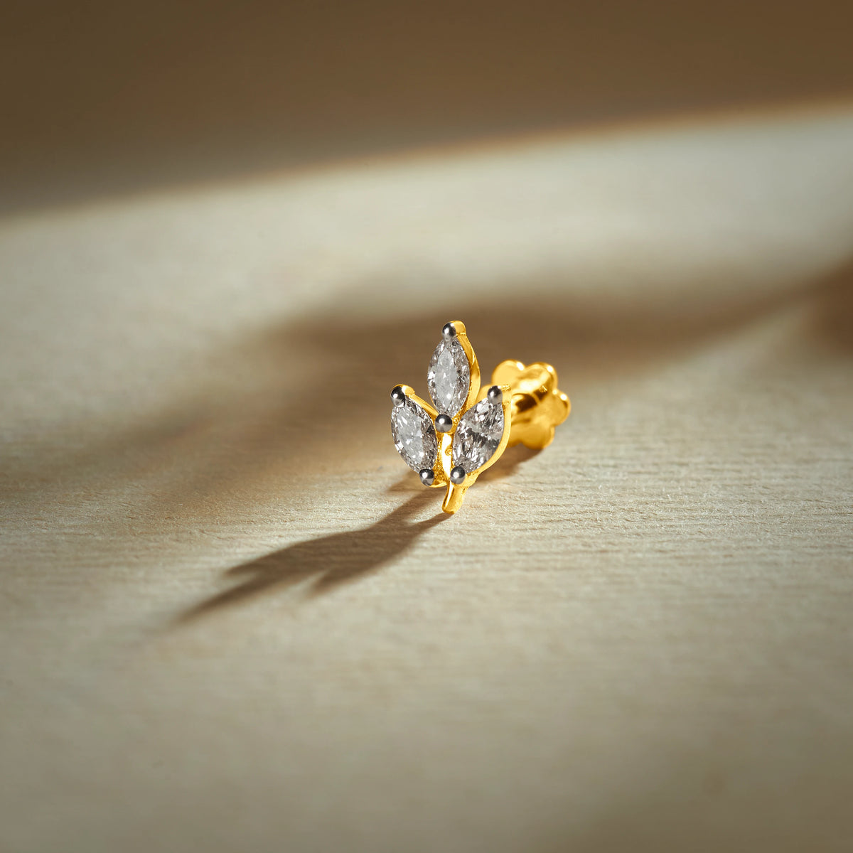 Flower nose pin gold with leaf-inspired floral design featuring sparkling marquise stones set in a polished gold base on a soft neutral background