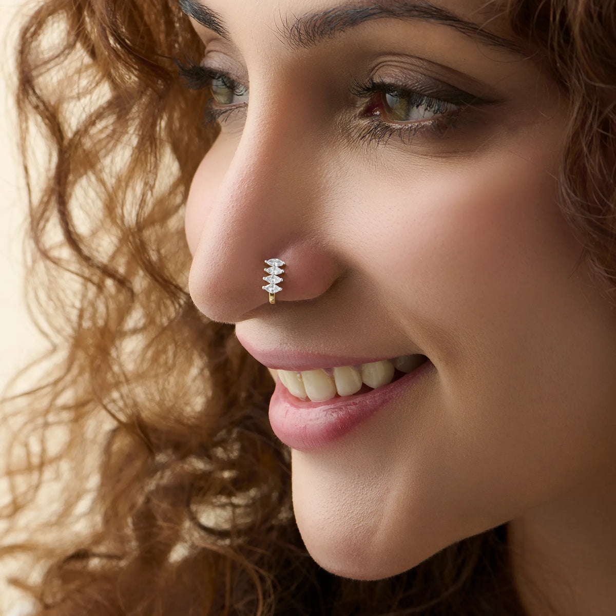 Smiling woman wearing a stylish gold J type nose pin with shiny white stones.