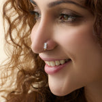 Smiling woman wearing a stylish gold J type nose pin with shiny white stones.