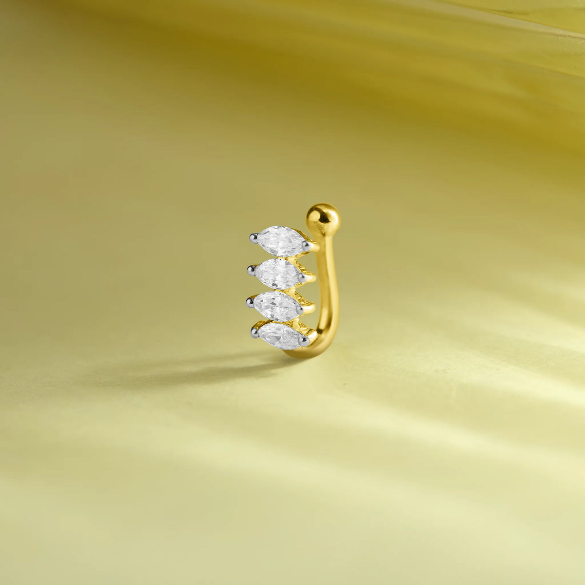 J type gold nose pin with three marquise-cut sparkling white stones on a soft pastel green background.