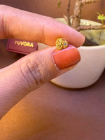 Round mesh-textured gold nose pin with black stone accent, held between fingertips