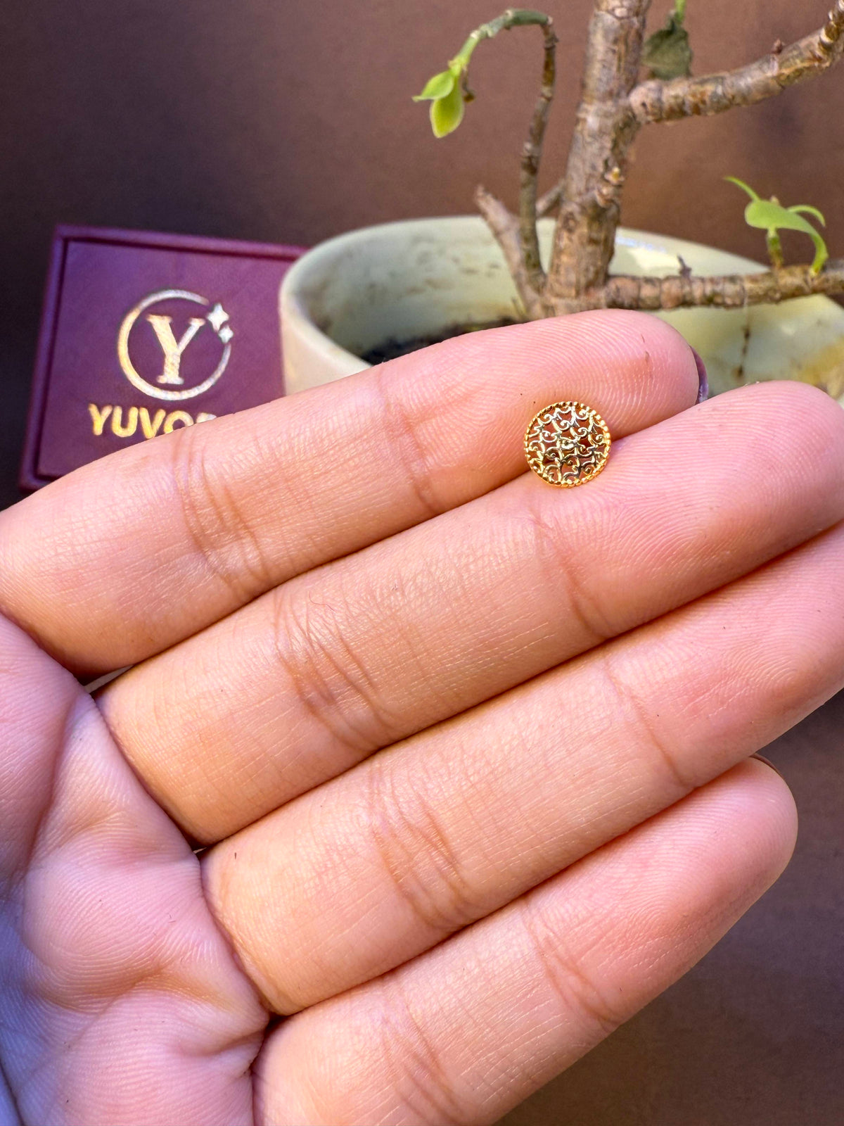 Round gold nose pin with mesh textured dome, held in hand