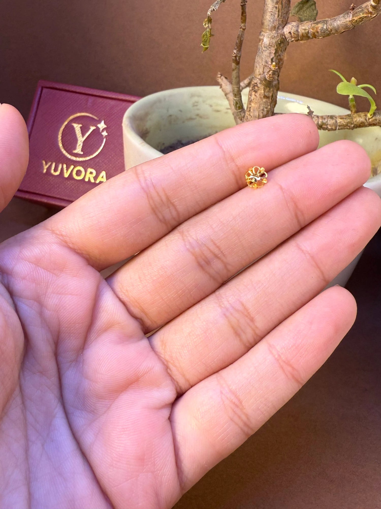 Small round gold flower nose pin with plain finish held in hand, Yuvora jewelry box in background