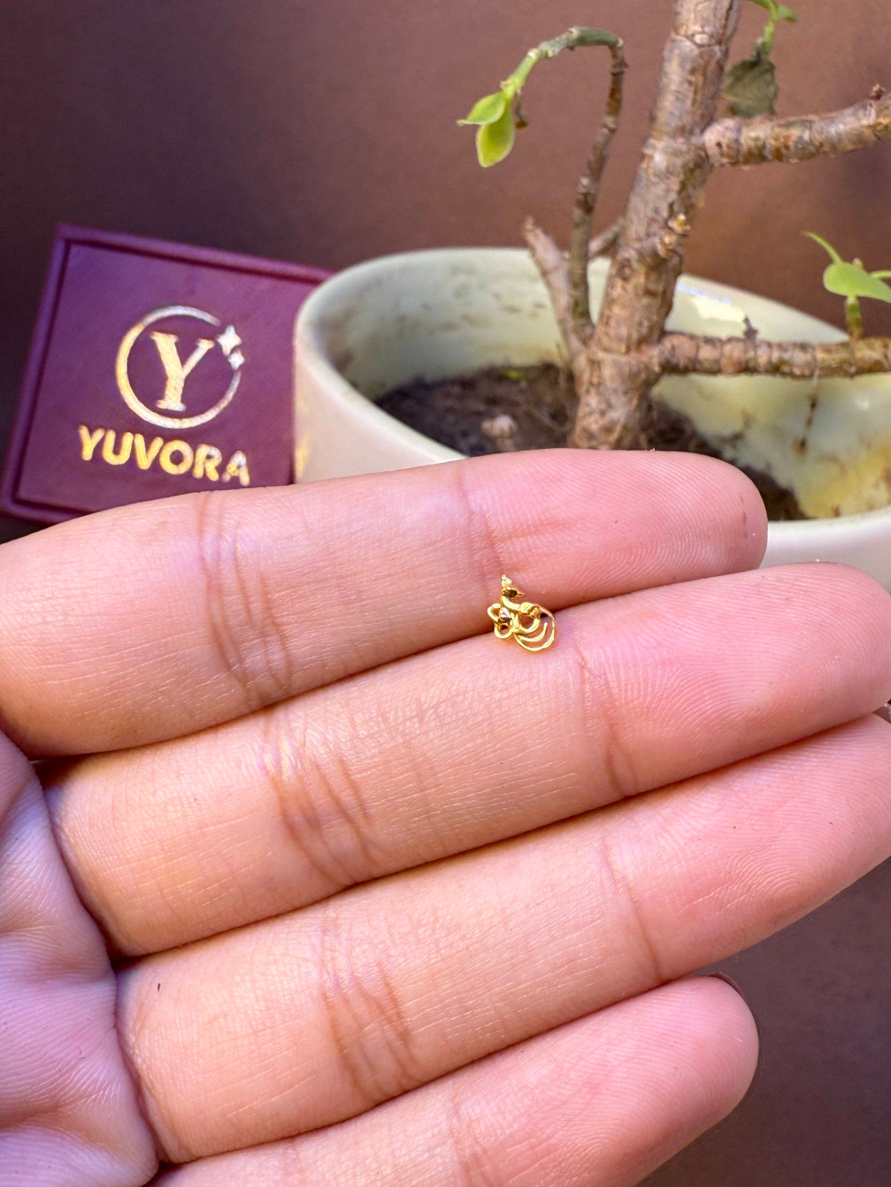 Small mango motif gold nose pin with delicate curves, held in hand