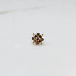 A gold nose pin shaped like a flower, set with multicolored gemstones in shades of red, blue, green, and purple