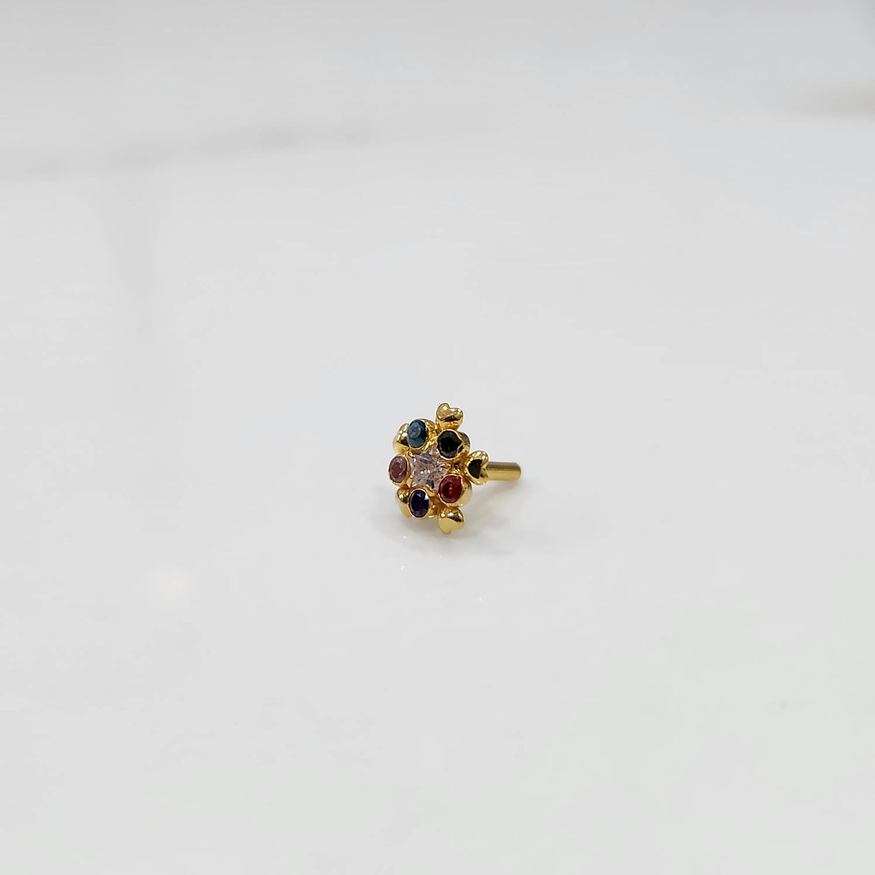 Product shot of a gold nose stud with multicolor gemstone flower cluster