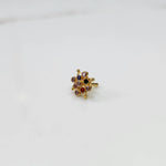 A gold nose pin shaped like a flower, set with multicolored gemstones including red, blue, and champagne tones
