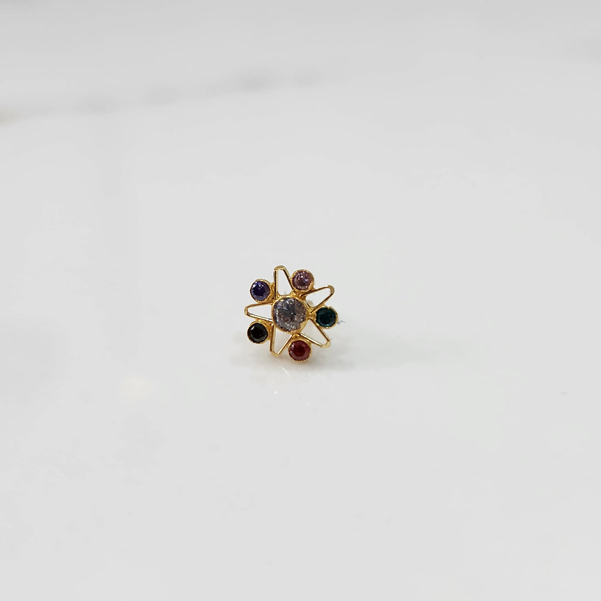 A gold nose pin shaped like a star with a pale grey center stone and multicolored accent stones in purple, pink, green, black, and red