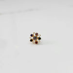 A gold nose pin shaped like a star with a pale grey center stone and multicolored accent stones in purple, pink, green, black, and red