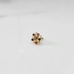 A gold nose pin shaped like a star with a soft pink center stone and multicolored accent stones in purple, green, and red