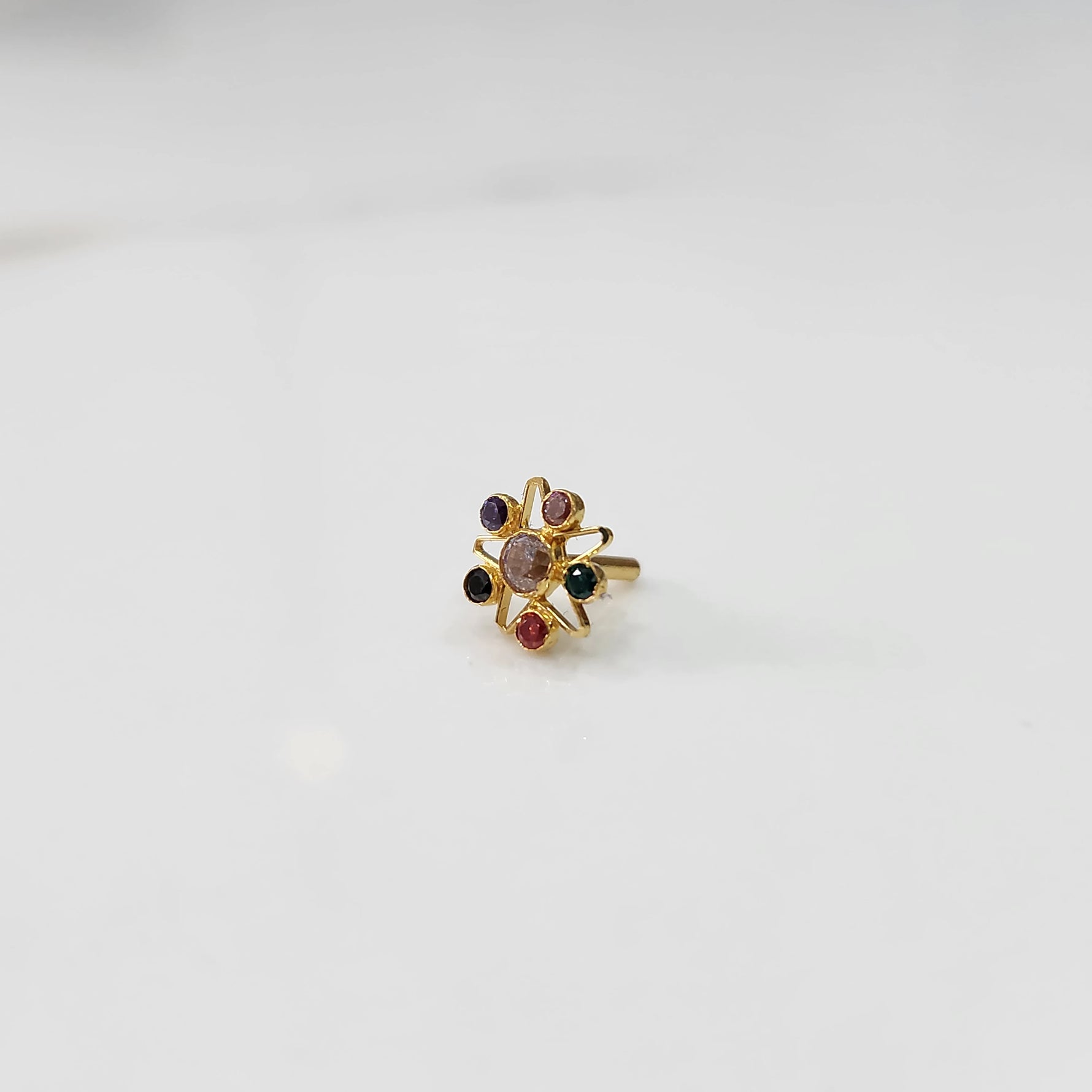 A gold nose pin shaped like a star with a soft pink center stone and multicolored accent stones in purple, green, and red