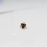 An 18K gold nose pin shaped like a flower, set with multicolored stones in teal, purple, red, and blue, each in an open gold loop