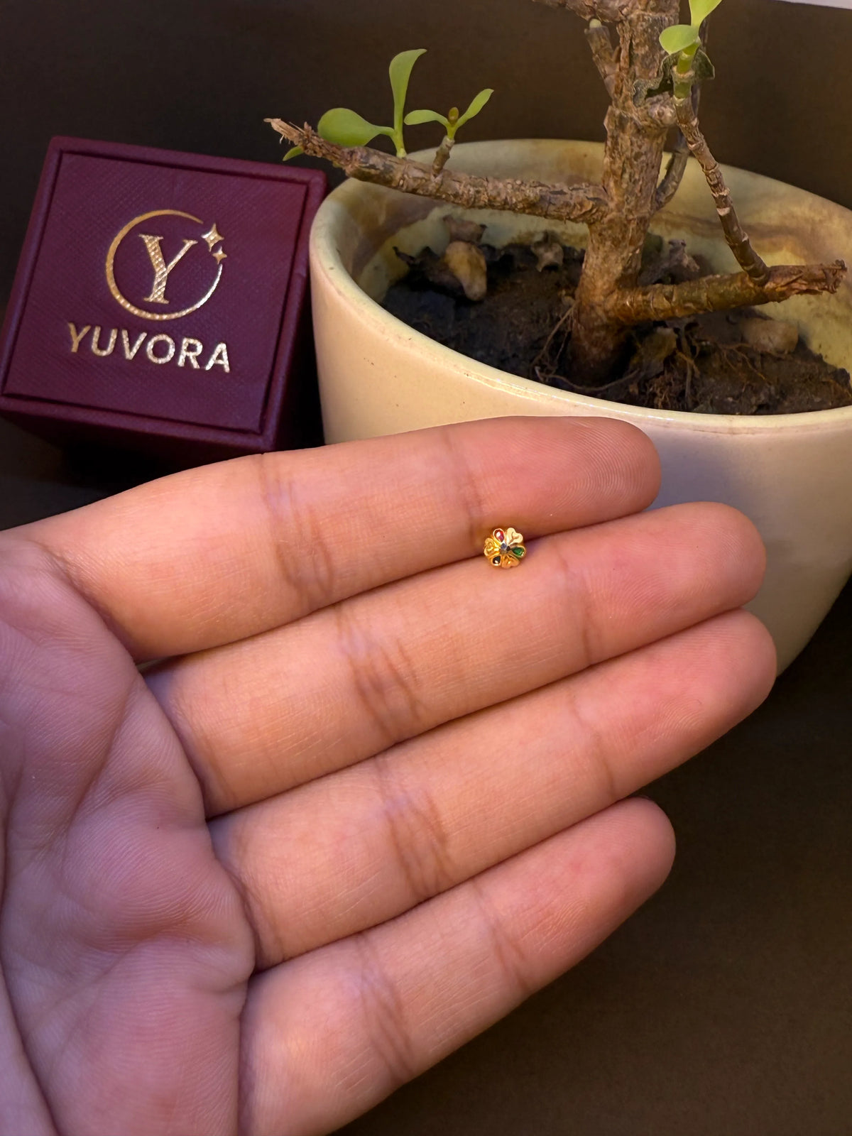 Gold nose pin with multicolor stone flower pattern, held in hand