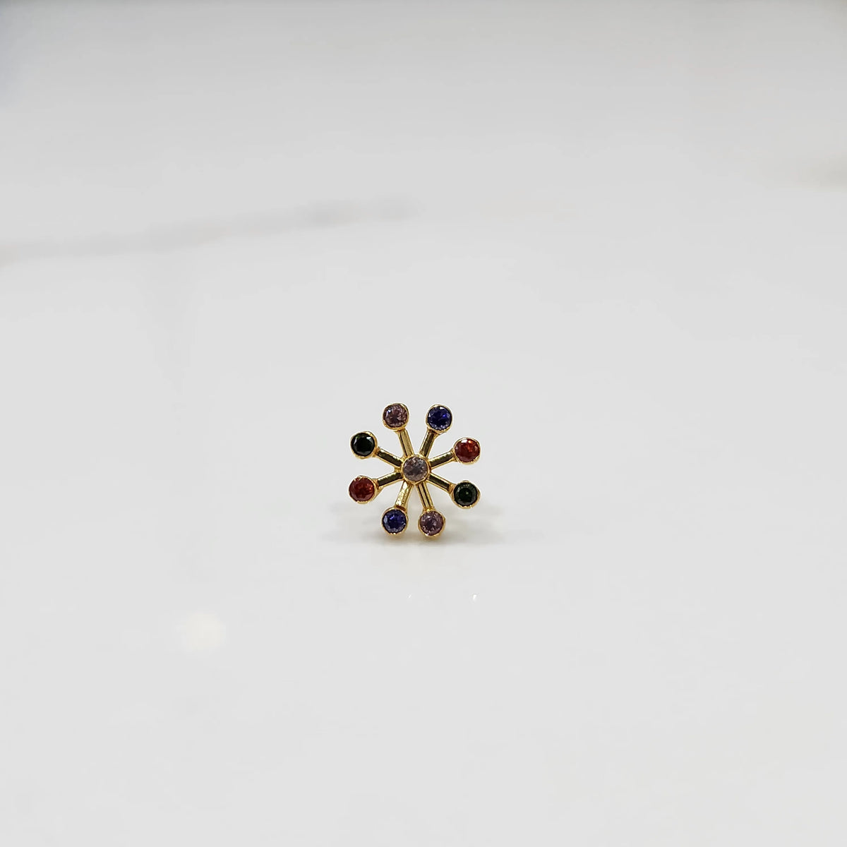 Product shot of a gold nose stud with nine multicolor navratna gemstones