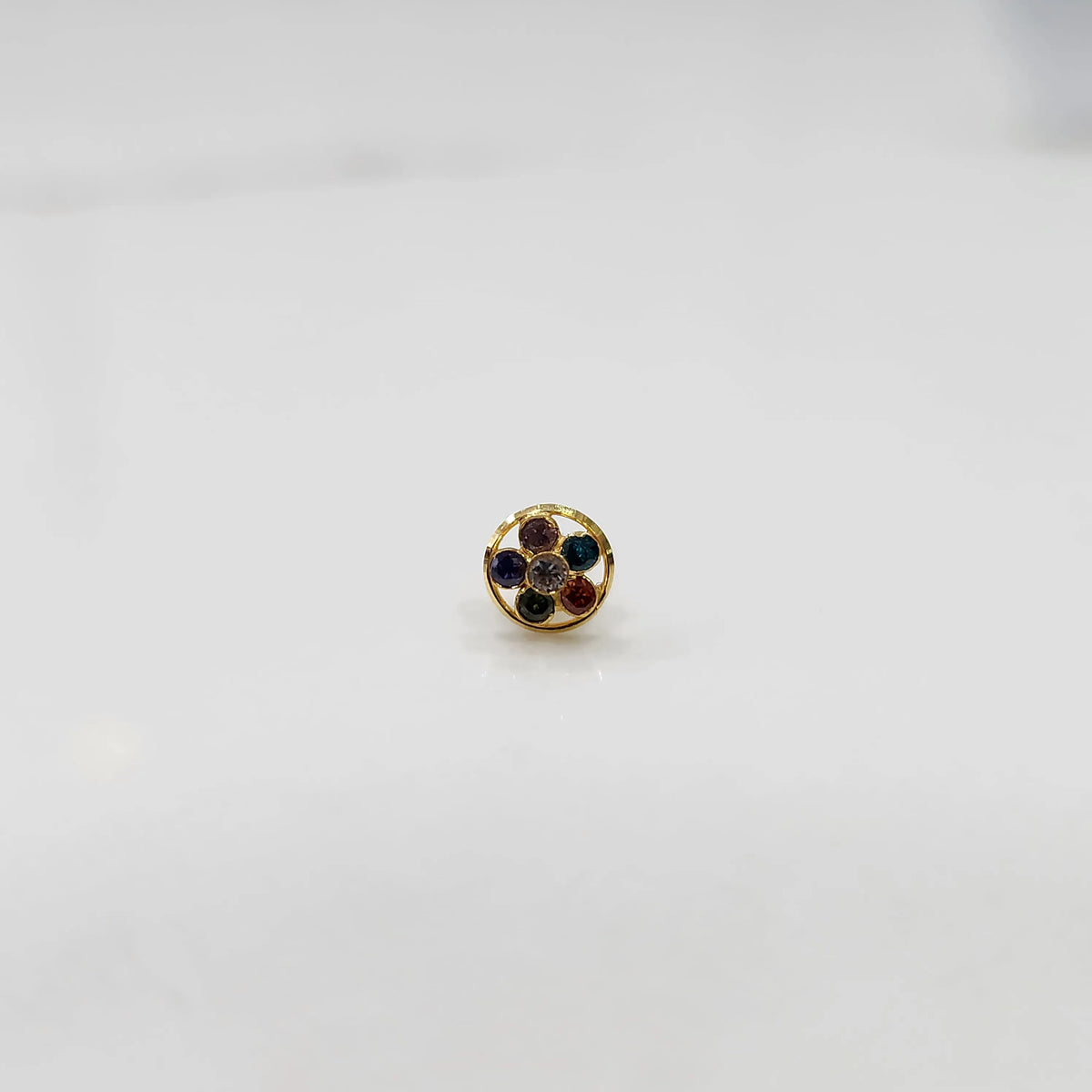 Product shot of a round gold nose stud with navratna multicolor gemstones