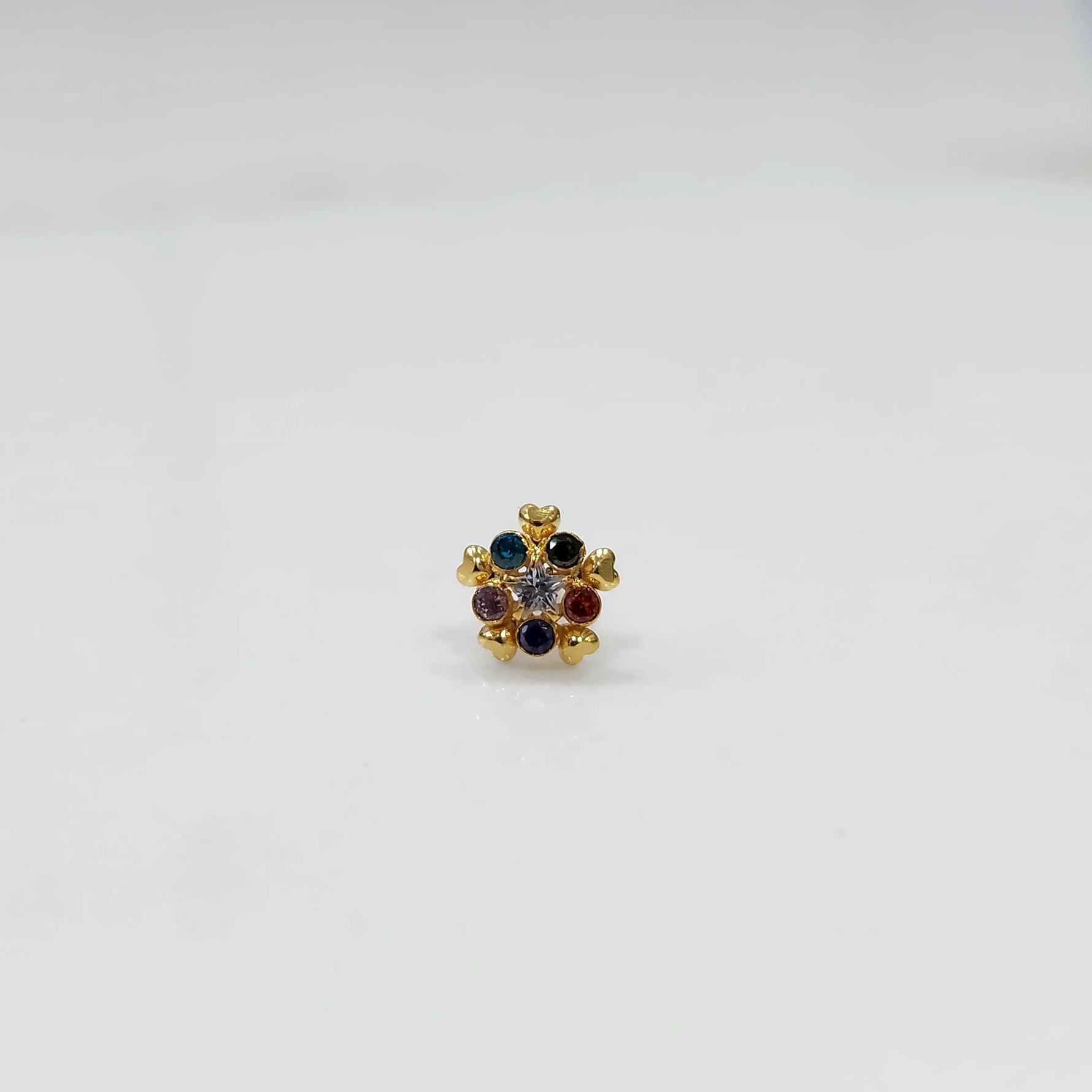 Close-up of a navratna-style nose pin with red, blue, and clear stones