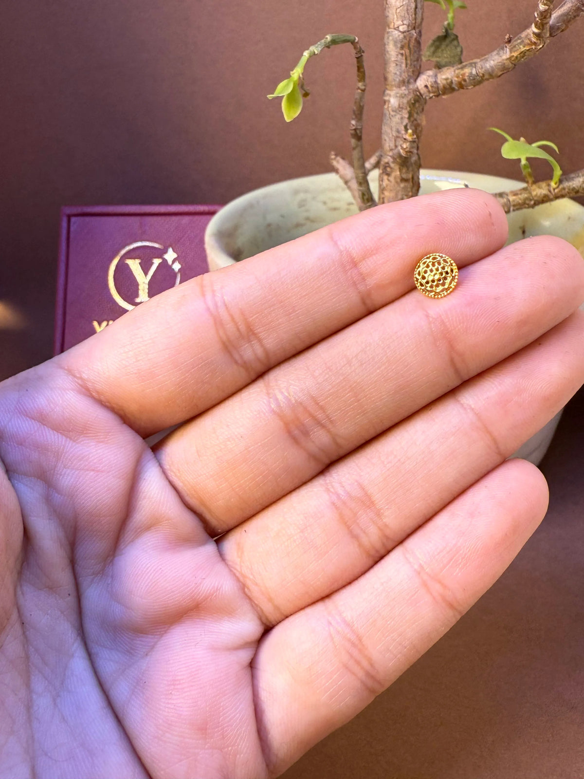Round gold nose pin with fine net-lattice textured dome, held in hand