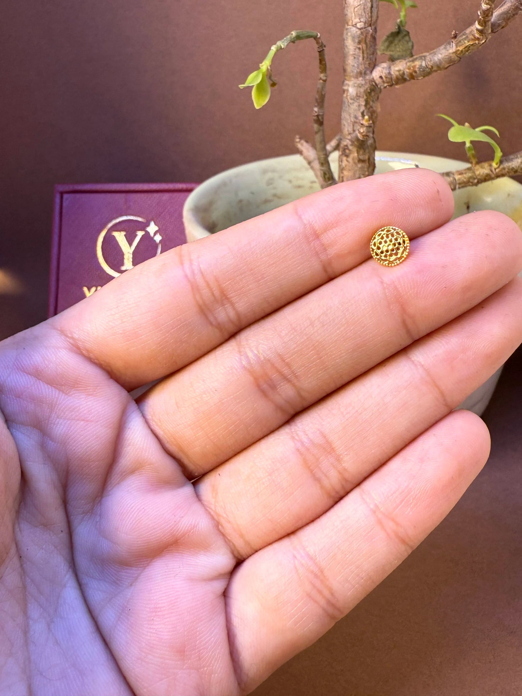 Round gold nose pin with fine net-lattice textured dome, held in hand