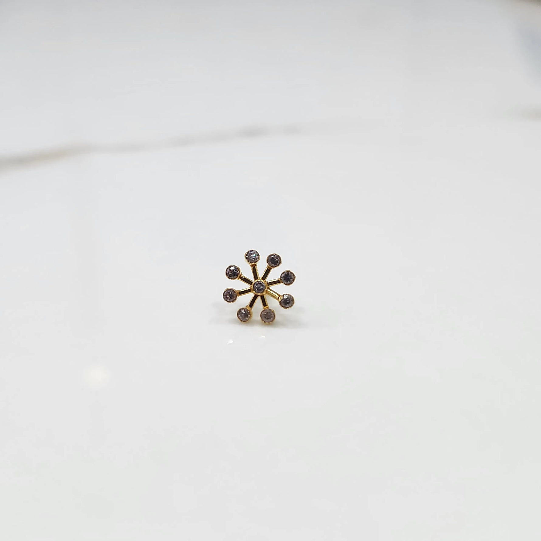 Product shot of a gold nose stud with a nine-diamond sunburst flower design