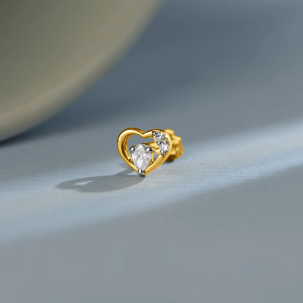 Gold heart outline stud earring featuring a pear diamond and round accent stones