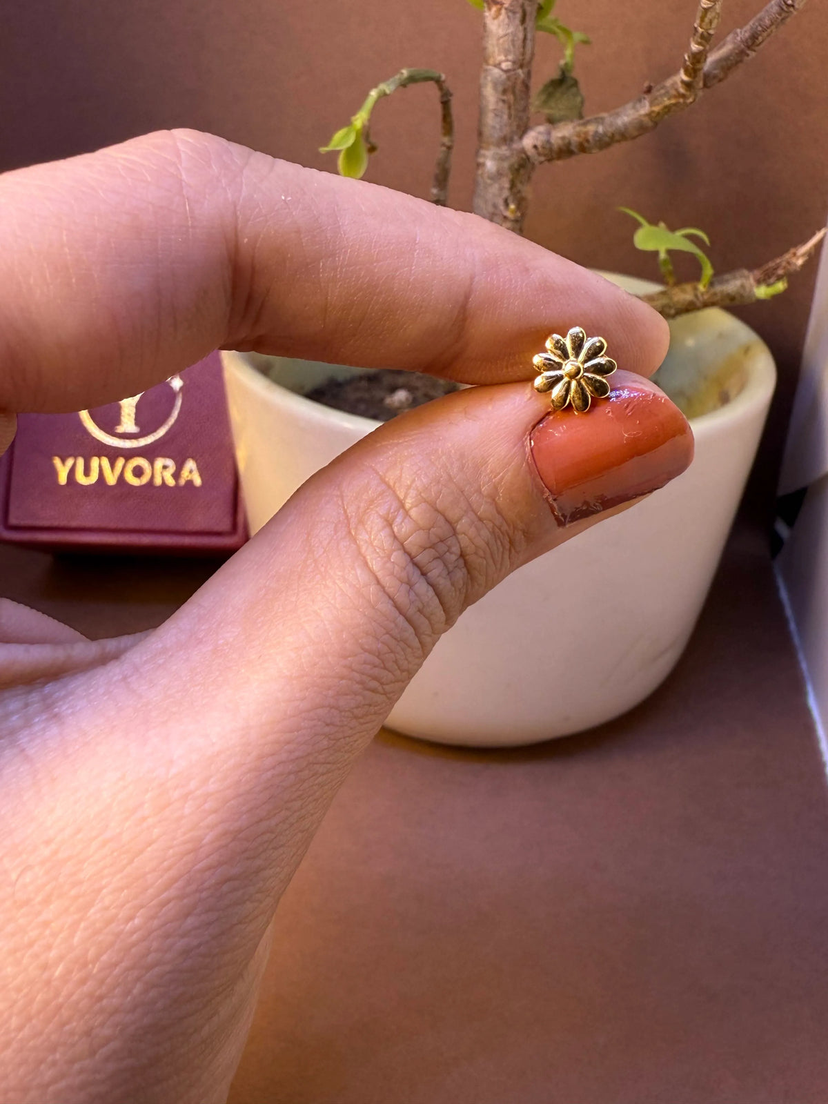 Simple daisy-shaped gold nose pin with antique oxidized finish, held between fingertips