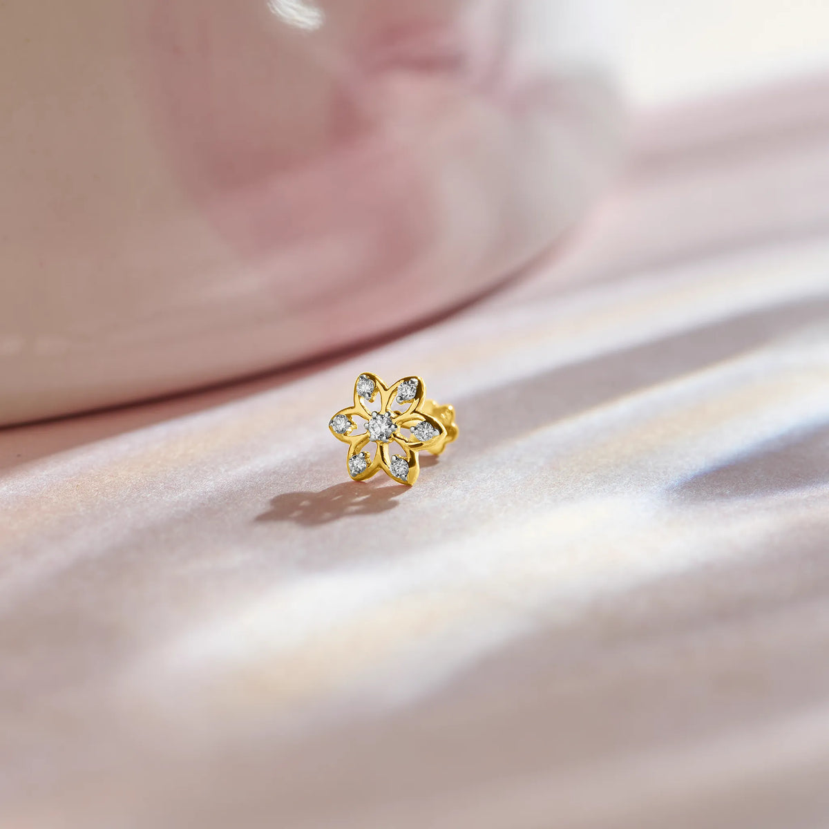 Flower nose pin gold with delicate floral design featuring sparkling stones set in a polished gold base on a soft pink satin background