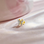 Design of gold nose pin with butterfly shape and diamond detailing on soft pink fabric background