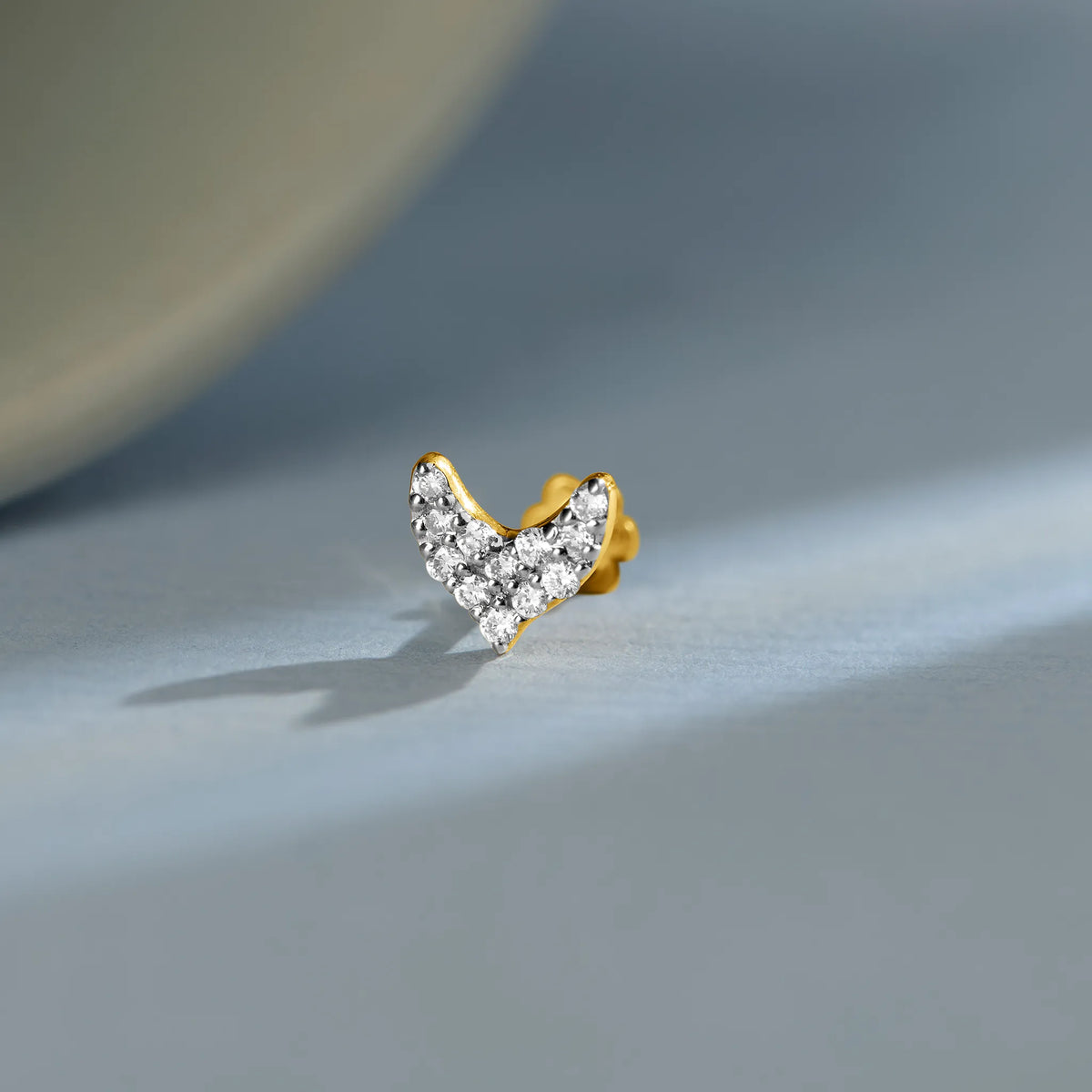 Gold V-shaped diamond nose pin design on soft blue background