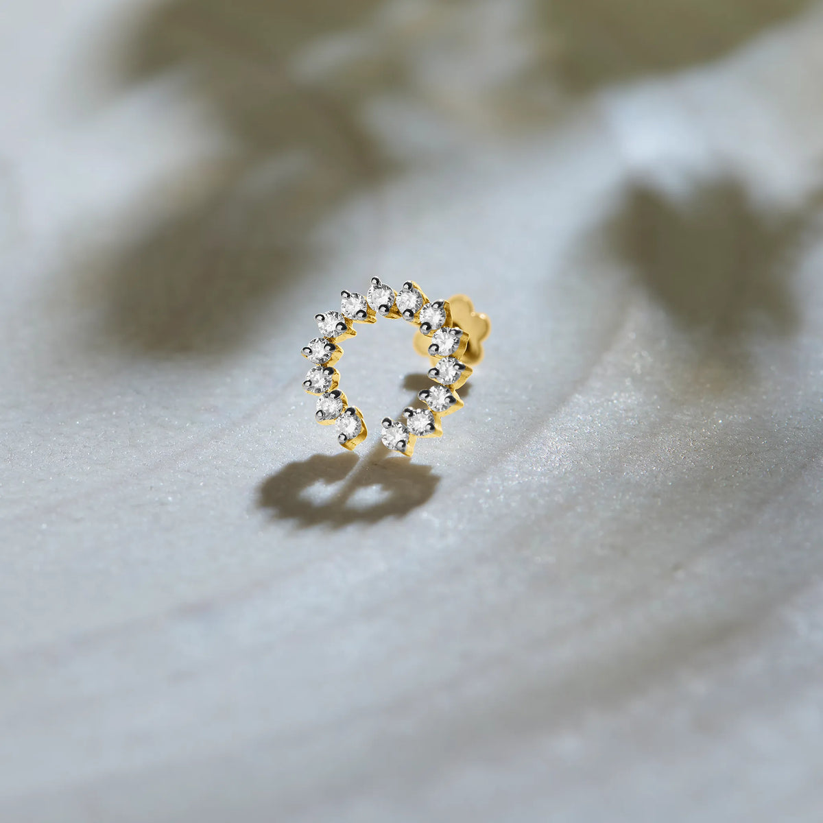 Gold circular diamond nose pin design on textured white background