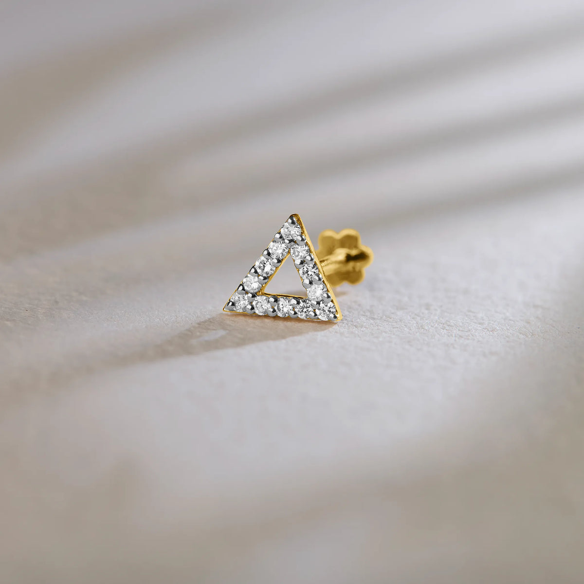 Fancy gold triangle nose pin with diamond detailing on soft background