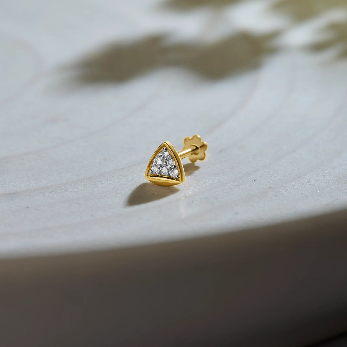 Gold triangle diamond nose pin on soft textured background