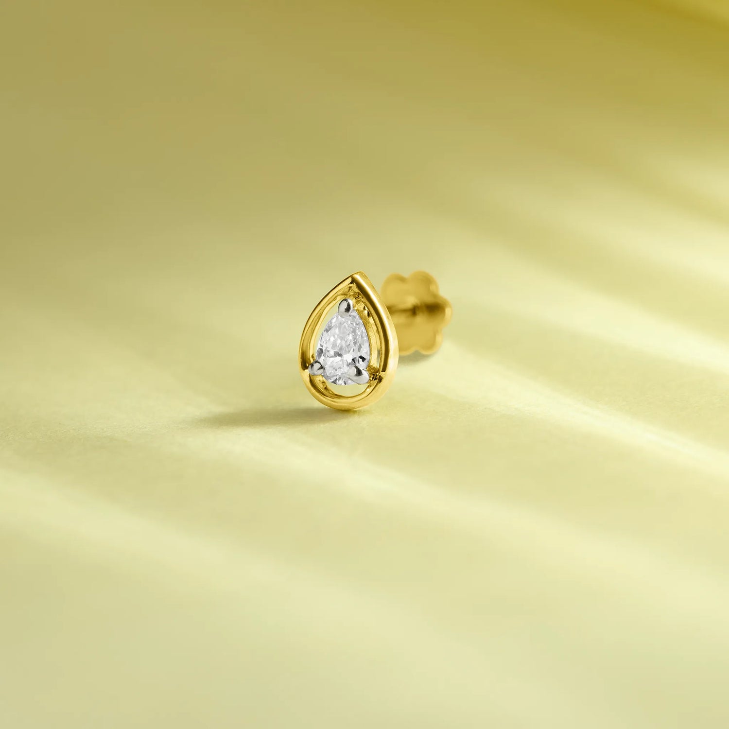 Gold teardrop diamond nose pin on soft pastel background