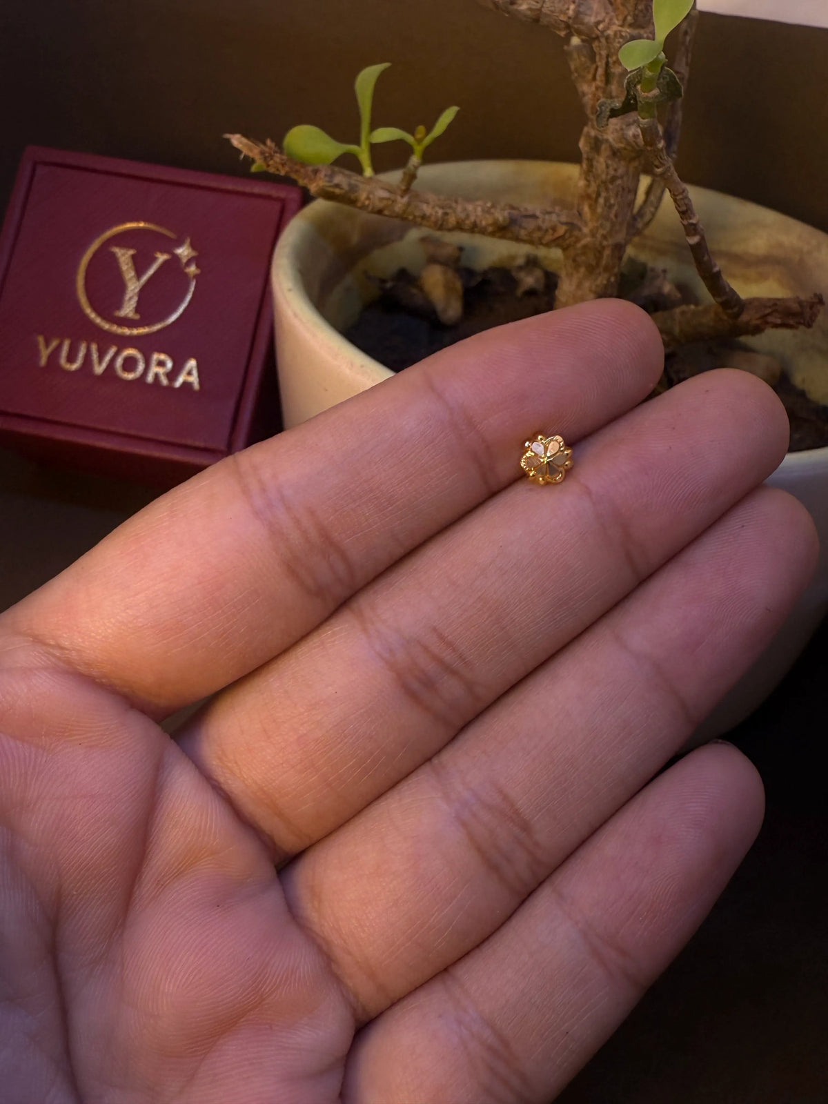Small daisy-shaped gold nose pin with center stone, held in hand