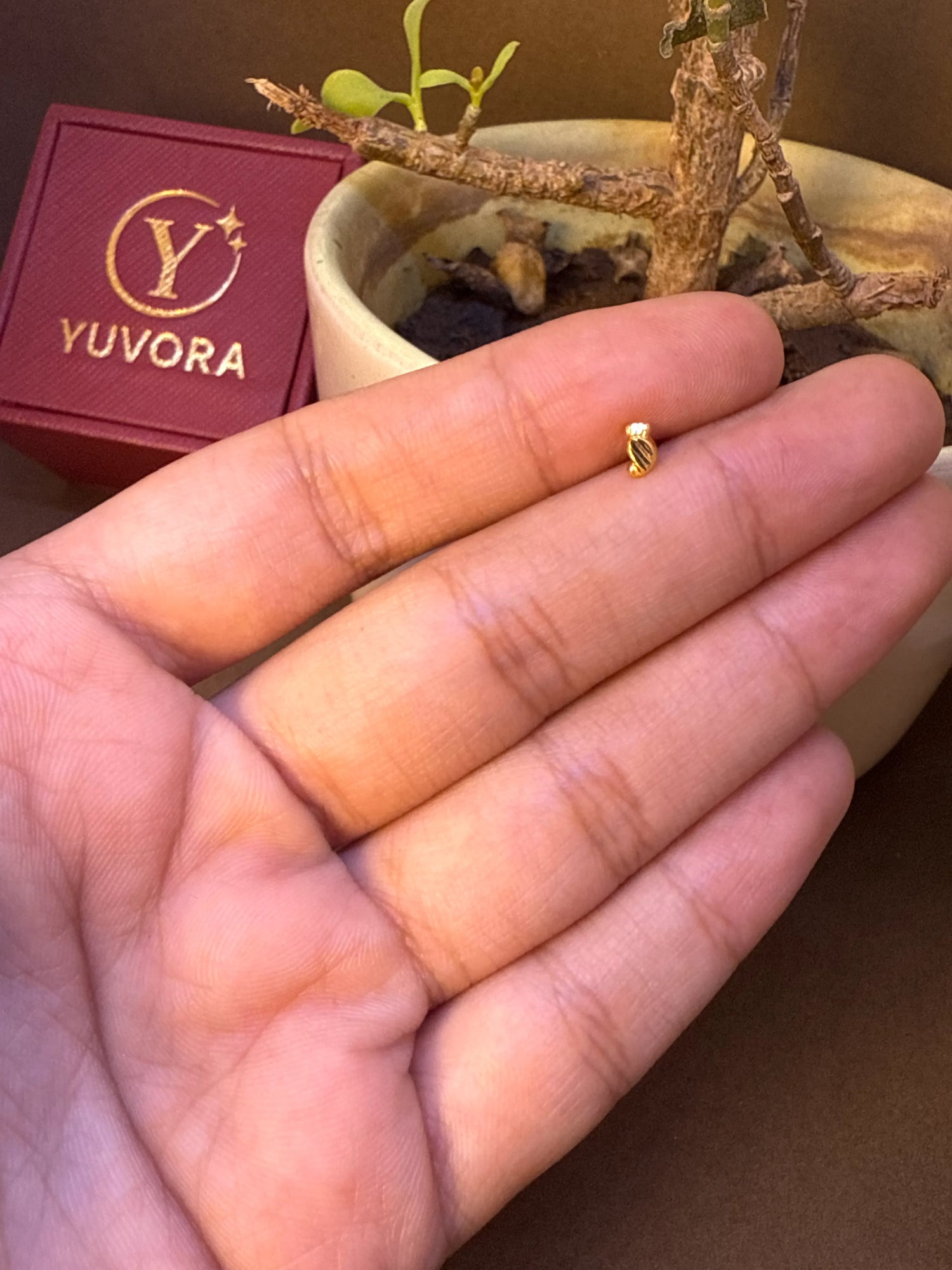 Plain curved gold nose pin stud resting on fingers, side angle view