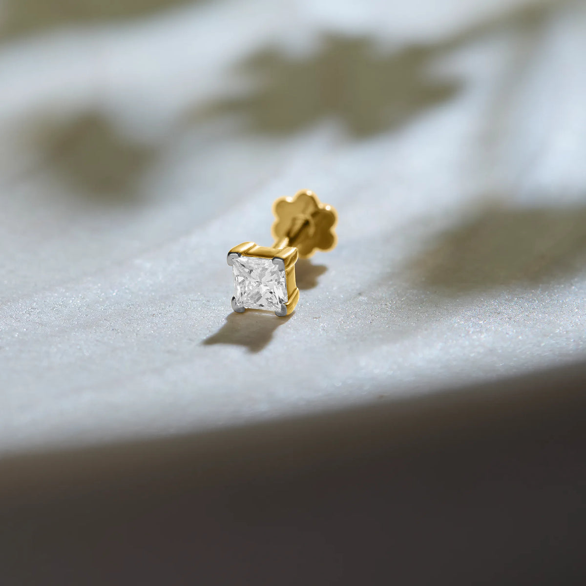 Diamond nose pin design from Kerala in gold with square solitaire diamond on textured background