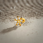 An 18K gold nose pin shaped like a wheel with pointed gold spokes between clear crystal stones, photographed on a light textured surface