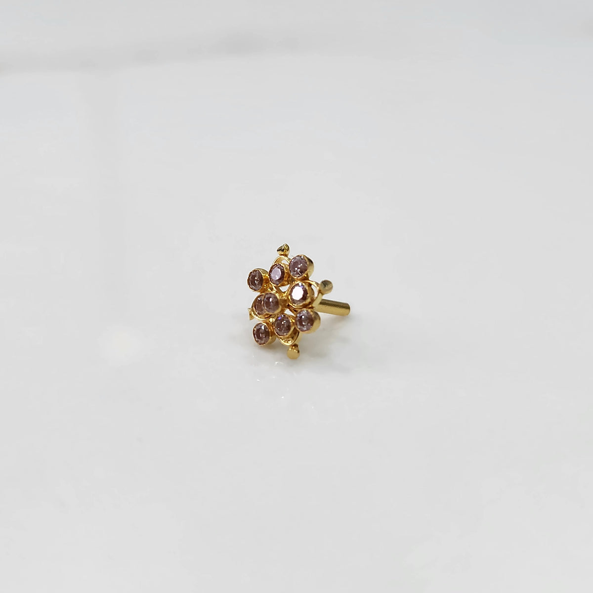 A gold nose pin shaped like a flower, set with soft pink-brown crystal stones