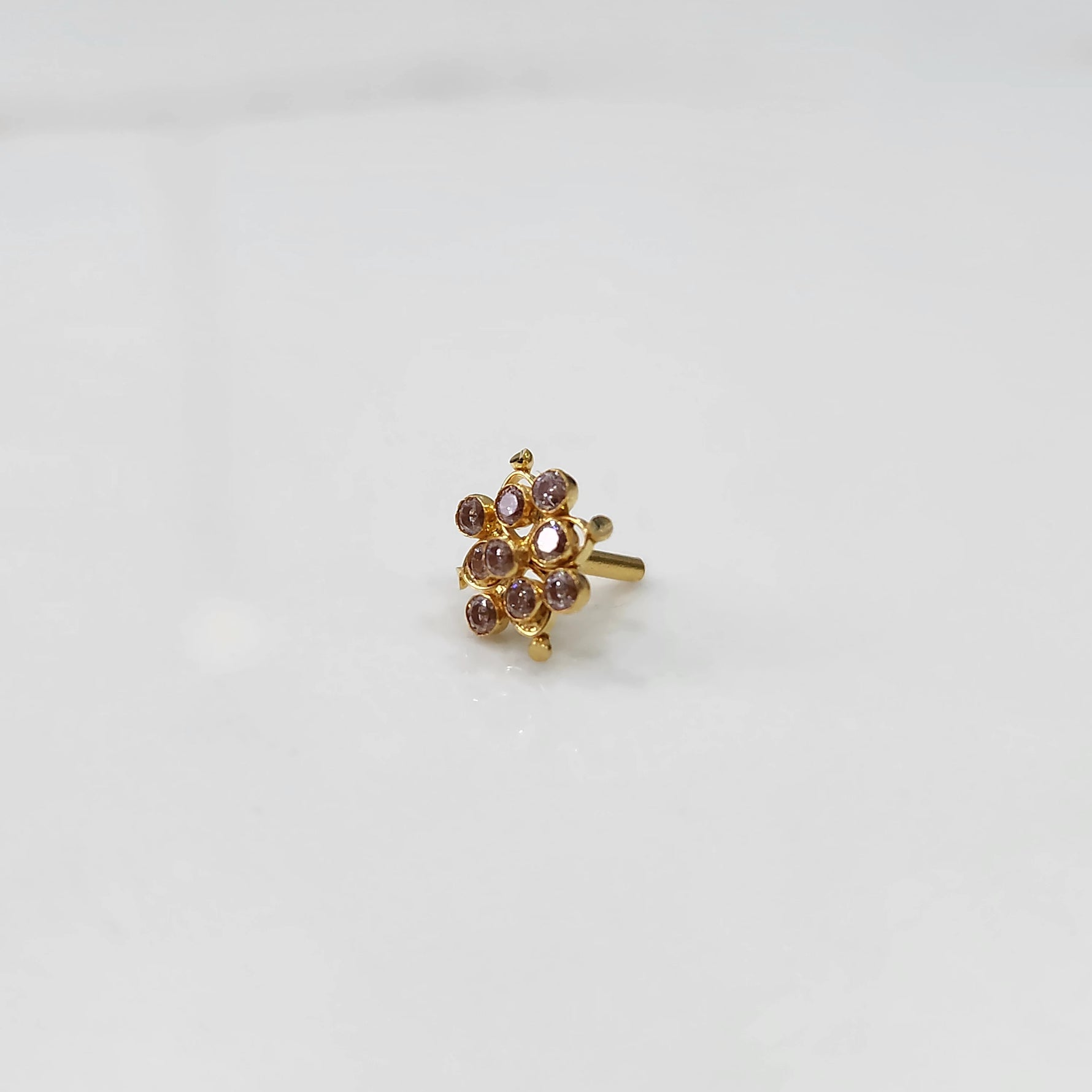 A gold nose pin shaped like a flower, set with soft pink-brown crystal stones