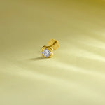 Elegant gold flower nose pin with a sparkling round stone placed on a soft pastel green background.
