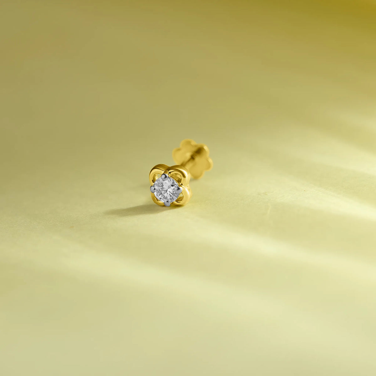 Elegant gold flower nose pin with a sparkling round stone placed on a soft pastel green background.